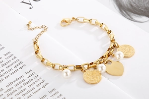 Détail d'un bracelet en acier doré avec perles, médailles et breloque en cœur