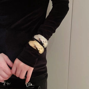 Close-up of chunky gold and silver oval bangles with mirror finish on black sleeves