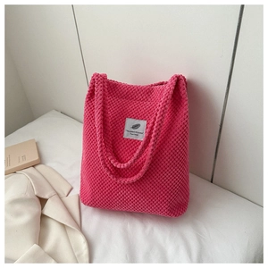Detailed close-up of a pink corduroy handbag with a white woven label on neutral fabric
