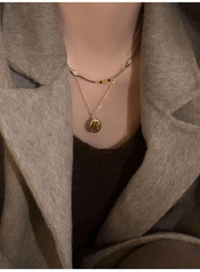 Detail of layered gold necklace featuring oval tiger eye pendant on a warm knit sweater