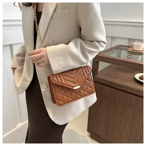 Detail of warm brown quilted crossbody bag with gold chain strap worn by a model