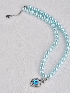 Detail of blue heart pendant and light blue pearl necklace on textured paper