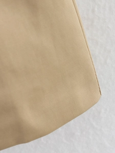 Close-up of khaki trench coat fabric showing fine twill texture and precision stitching