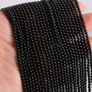 Close-up of polished 2mm black agate natural stone beads held by hand for DIY jewelry