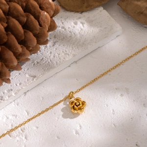 Macro view of golden camellia pendant necklace on stone background with natural decor