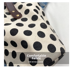 Detail of white canvas tote with black polka dots, brown leather handle, and gold rivets