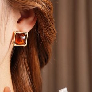 Close-up of amber resin square earring with gold metal frame worn by a model