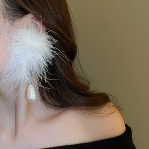 Detailed view of large white feather earrings with drop pearls on elegant model