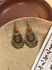 Détail de boucles d'oreilles vintage avec perles orange et glands sur plateau en céramique