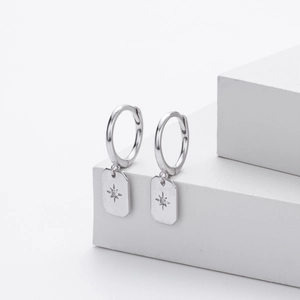 Macro detail of silver S925 drop earrings with star pattern and zircon on white stand