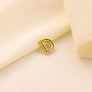 Gros plan d'un pendentif lettre D doré poli posé sur un tissu de soie beige doux