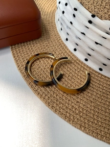 Detail of tortoise shell resin C-shaped hoop earrings with gold metal lining on straw hat