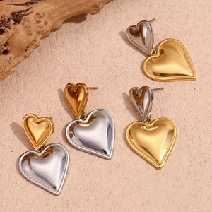 Flat lay of double-layer heart earrings in gold and silver finish on textured background