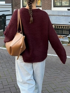 Close-up of a brown leather shoulder bag worn by a model in a modern urban street setting