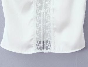 Close-up of white satin top featuring delicate lace splicing and a small white button