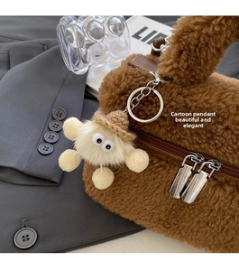 Detail view of brown plush bucket bag with cute cartoon doll charm and metal zippers