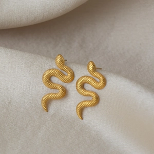 Boucles d'oreilles serpent dorées avec texture écaillée sur tissu beige minimaliste