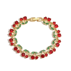 Elegant gold cherry bracelet featuring red and green crystal gemstones on white background