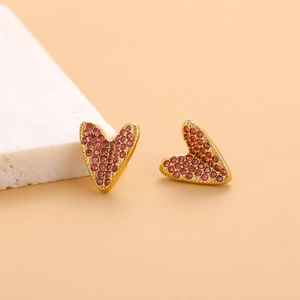 Macro detail of heart-shaped gold stud earrings with pink zircon on marble block
