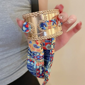 Close-up of wide gold cuff bracelet featuring embossed floral patterns and silk scarf wrap