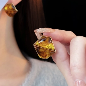 Macro view of geometric resin earrings in gold frames with amber tones on ear
