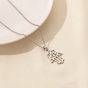 Detail view of silver stainless steel Hamsa hand pendant on a ceramic dish background