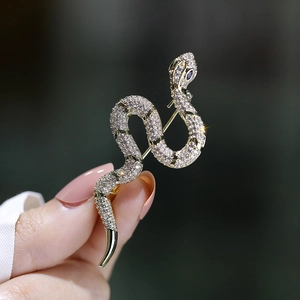 Elegant gold snake brooch with clear zircons and black eyes held by a hand