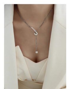 Silver-tone safety pin necklace with pearls and fringe pendant on a model in a beige suit