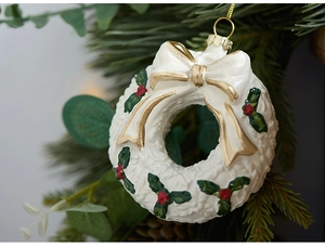 Close-up of cream Christmas wreath ornament with gold bow and holly berry relief details
