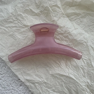 Detailed view of a pink translucent curved hair claw clip on a minimalist textured surface