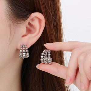 Macro view of multi-layered silver beaded stud earrings worn on ear showing fine metal details