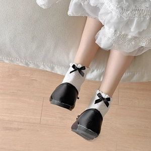 Close-up of white lace ruffle socks with black ribbon bow and black ballet flat shoes