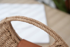Macro detail of hand-woven straw tote handle with twisted rope texture and leather accents