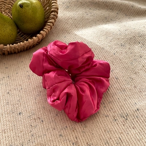 Gros plan d'un chouchou en soie rouge rose brillant sur un tissu en maille beige
