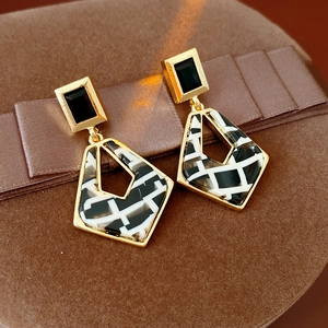 Close-up of geometric resin diamond-shaped earrings with gold metal and black square studs