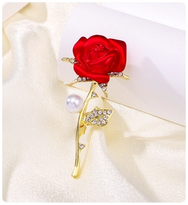 Close-up of elegant red rose brooch with rhinestones and pearl on silk fabric