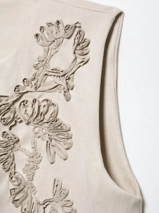 Close-up of beige embroidered vest showing detailed floral texture and fabric