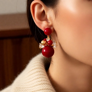 Detail of 18K gold plated round red bead drop earrings worn by a model on a brown background