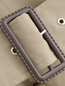 Detail of khaki twill fabric trench coat belt featuring brown textured buckle and metal pin
