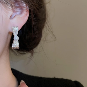 Orecchini a fiocco in argento con perla bianca indossati da modella su fondo caldo