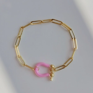 Detailed close-up of a gold chain bracelet featuring a pink enamel horseshoe buckle charm