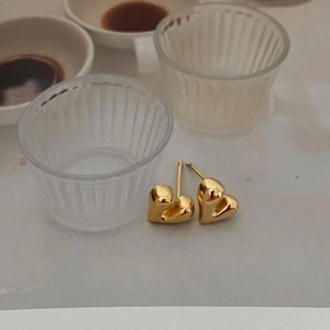 Close-up of minimalist gold heart-shaped stud earrings in a warm lifestyle setting