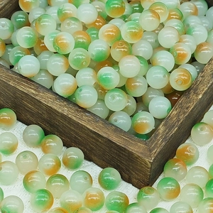 Macro detail of 8mm green and orange gradient glass beads in a wooden tray for DIY jewelry