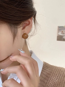 Detailed close-up of a glossy brown irregular pebble-shaped earring on model