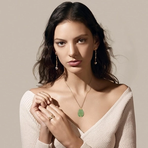 Detail of green enamel tree pendant with gold drop earrings and ring on a model