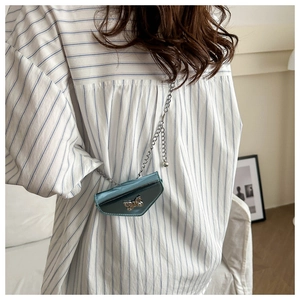 Detail of teal mini bow shoulder bag with silver chain worn over a blue striped shirt