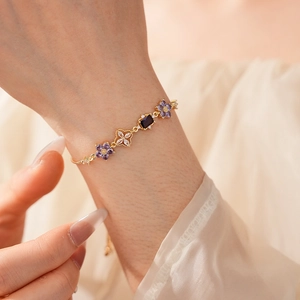 Detailed shot of gold chain bracelet with purple zircon flowers on a soft fabric backdrop