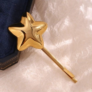 Macro detail of the 18K gold plated stainless steel star hair clip on a beige textured background