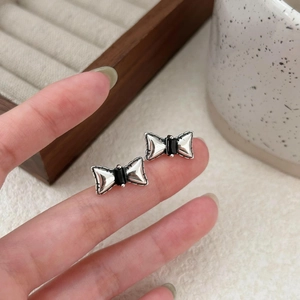 Close-up of bow knot earrings in silver with black rectangular zircon inlay held by hand