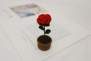 Close-up of a handmade crochet red rose in a brown knitted pot on an open book background